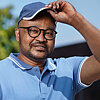 Eine Person mit schwarzer Brille, blauen Cap und blauen Polo-Shirt lächelt in die Kamera